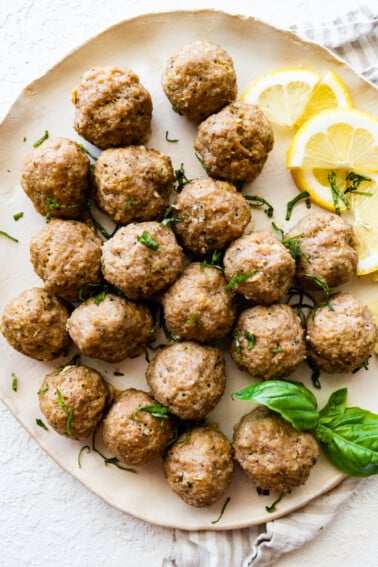 Baked turkey meatballs on a plate with fresh basil and lemon slices.
