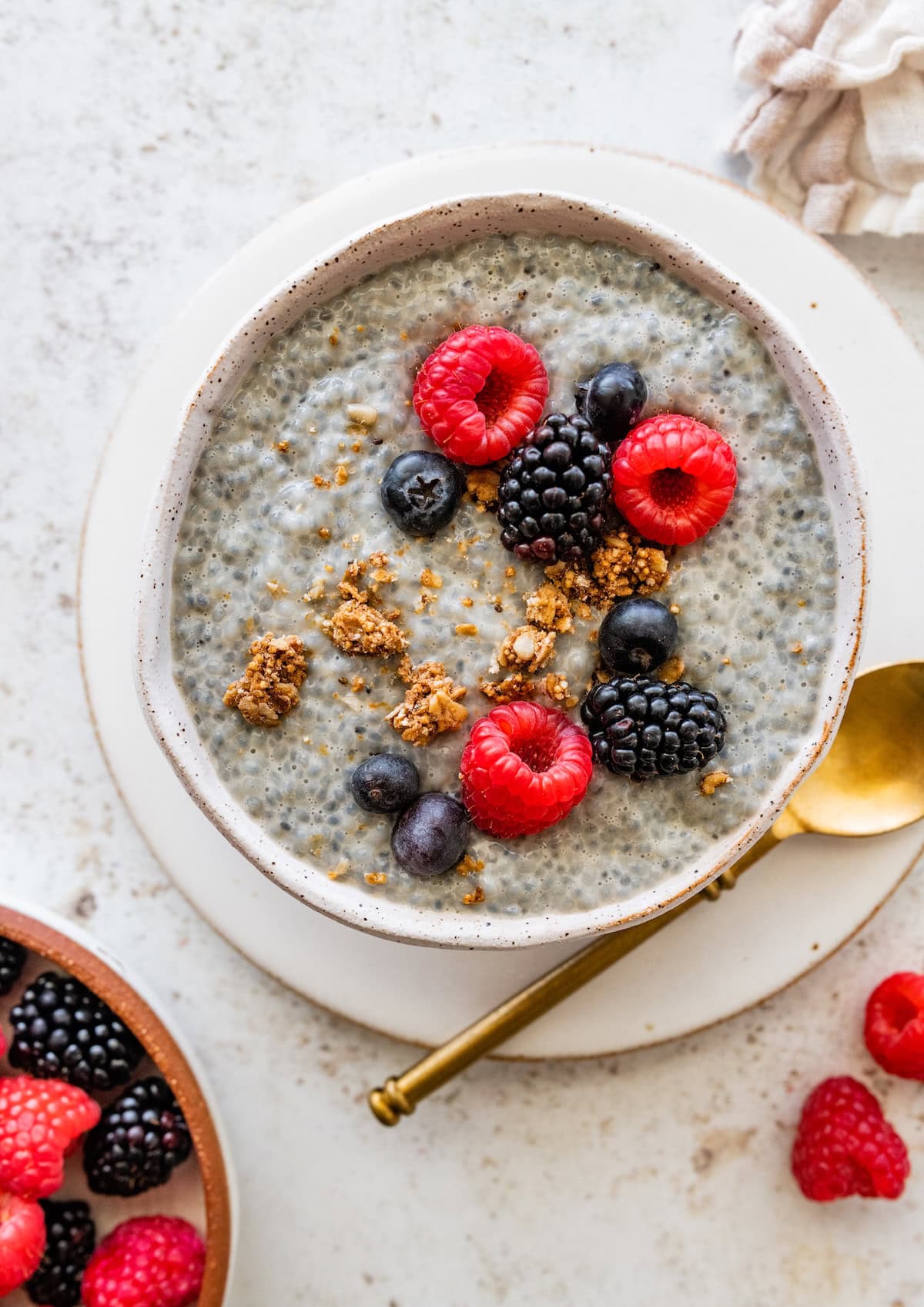 A bowl of basil seed pudding topped with raspberries and granola with a gold spoon