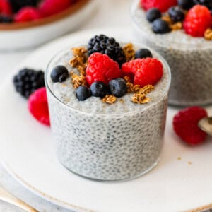 Glass of basil seed pudding topped with berries and granola on a white plate.