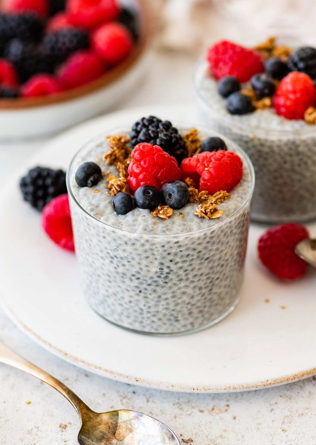 Glass of basil seed pudding topped with berries and granola on a white plate.