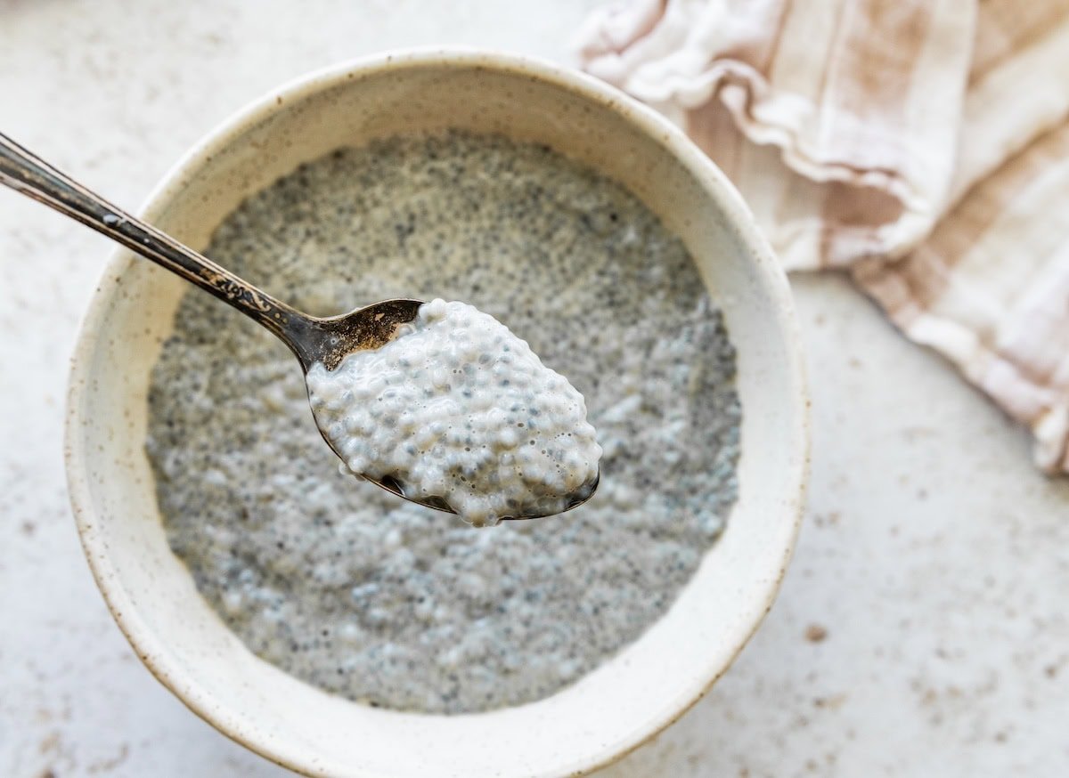 Spoon scooping thick basil seed pudding from a white bowl.