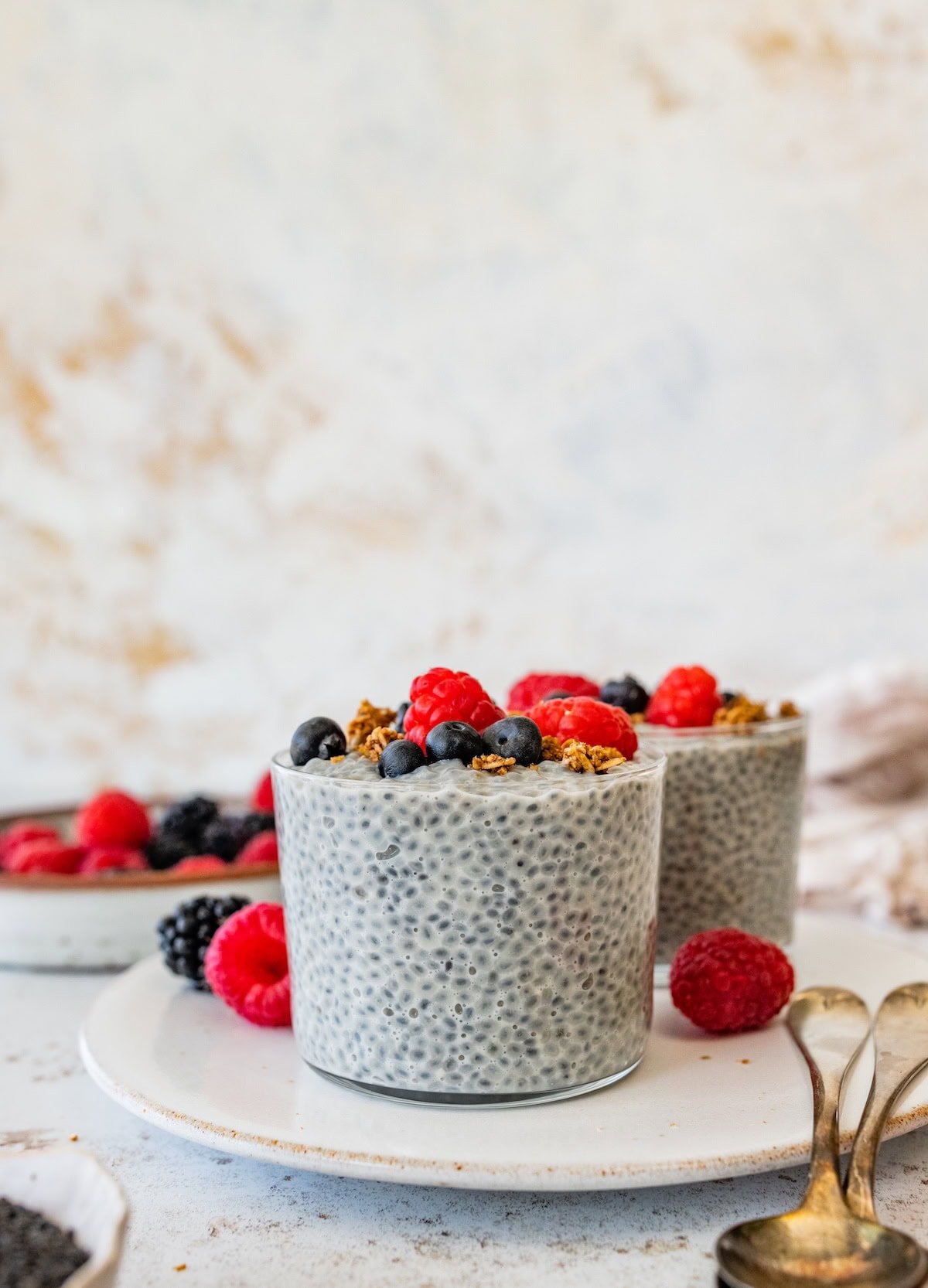 Glass of basil seed pudding topped with fresh berries on a white plate