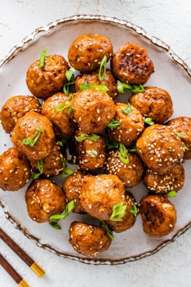 BBQ chicken meatballs on a plate topped with sesame seeds and sliced green onions.