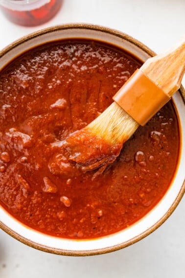 A bowl filled with homemade BBQ sauce with a small brush in the sauce.