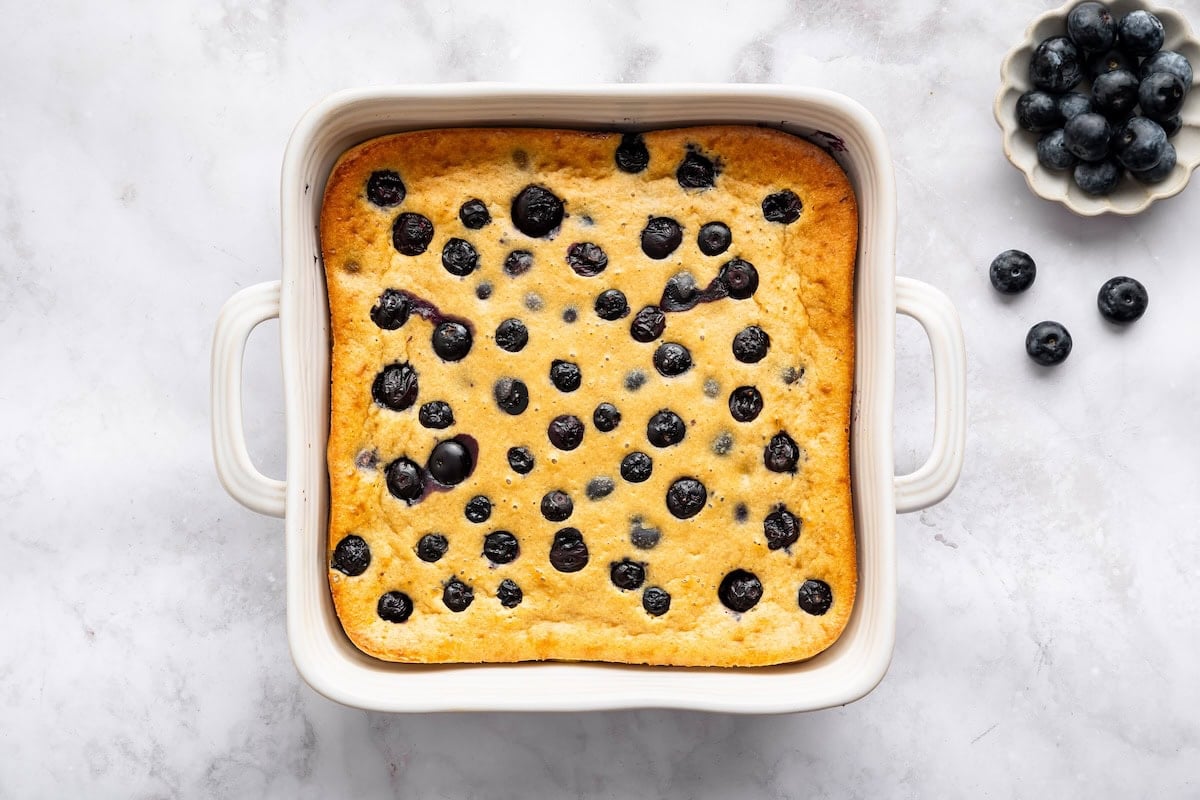 Freshly baked blueberry cottage cheese breakfast bake in a white square dish on marble surface.