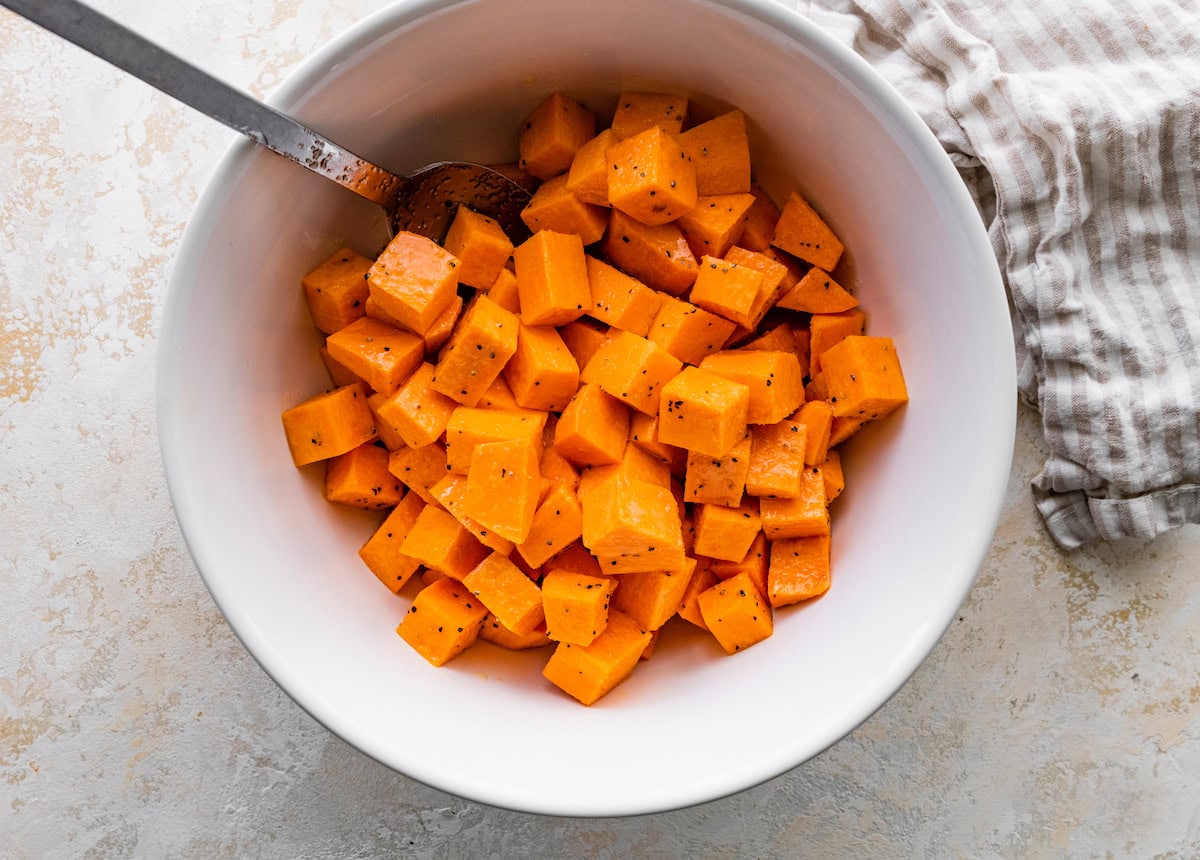 Chopped sweet potatoes in a white bowl tossed in oil, salt and pepper.