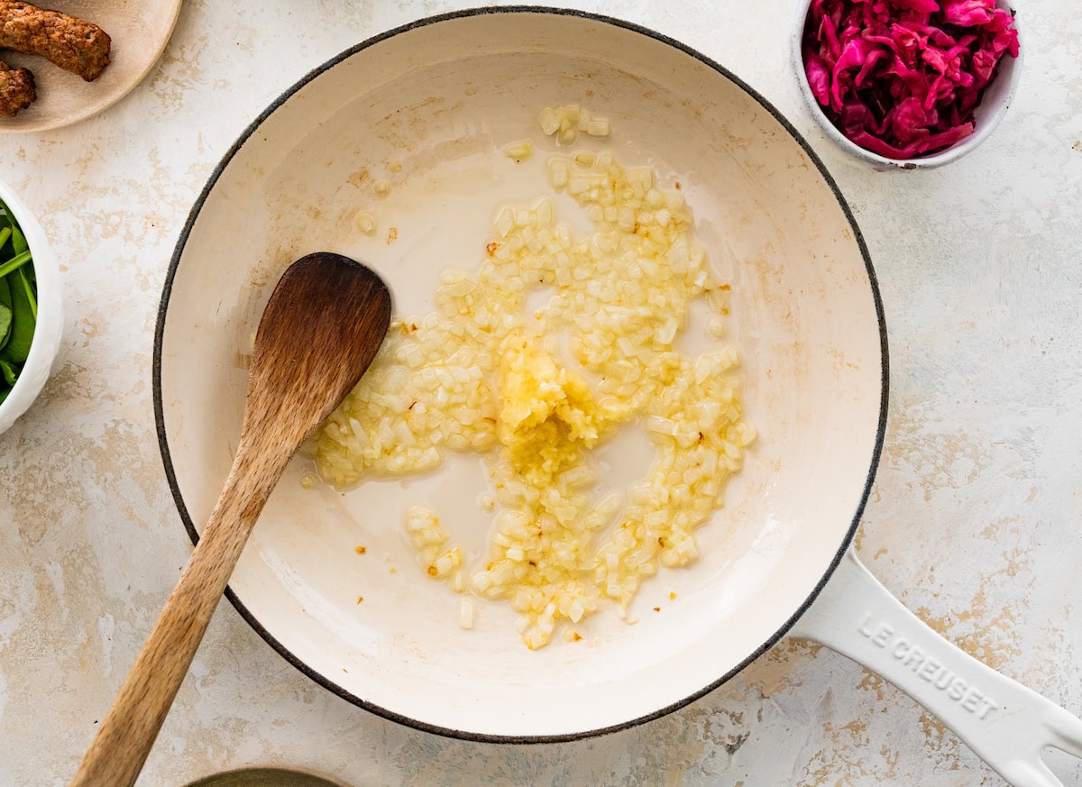 Sautéed onions and garlic cooking in a skillet with a wooden spoon.