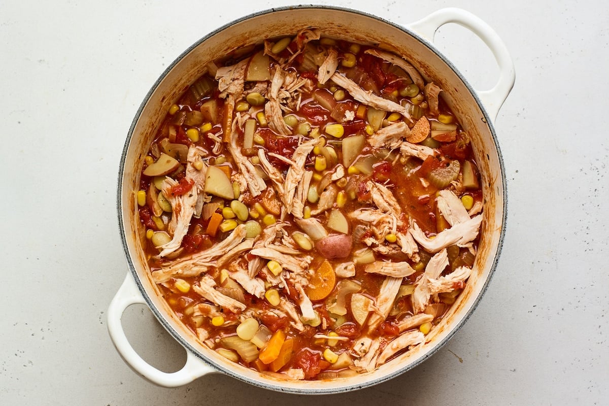 Shredded chicken added to a dutch oven containing Brunswick Stew.