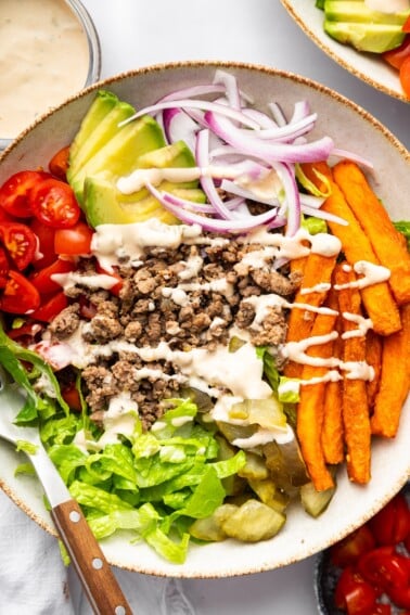 Assembled burger bowl with lettuce, tomato, onion, pickles, avocado, fries, and beef all drizzled with Big Mac sauce.