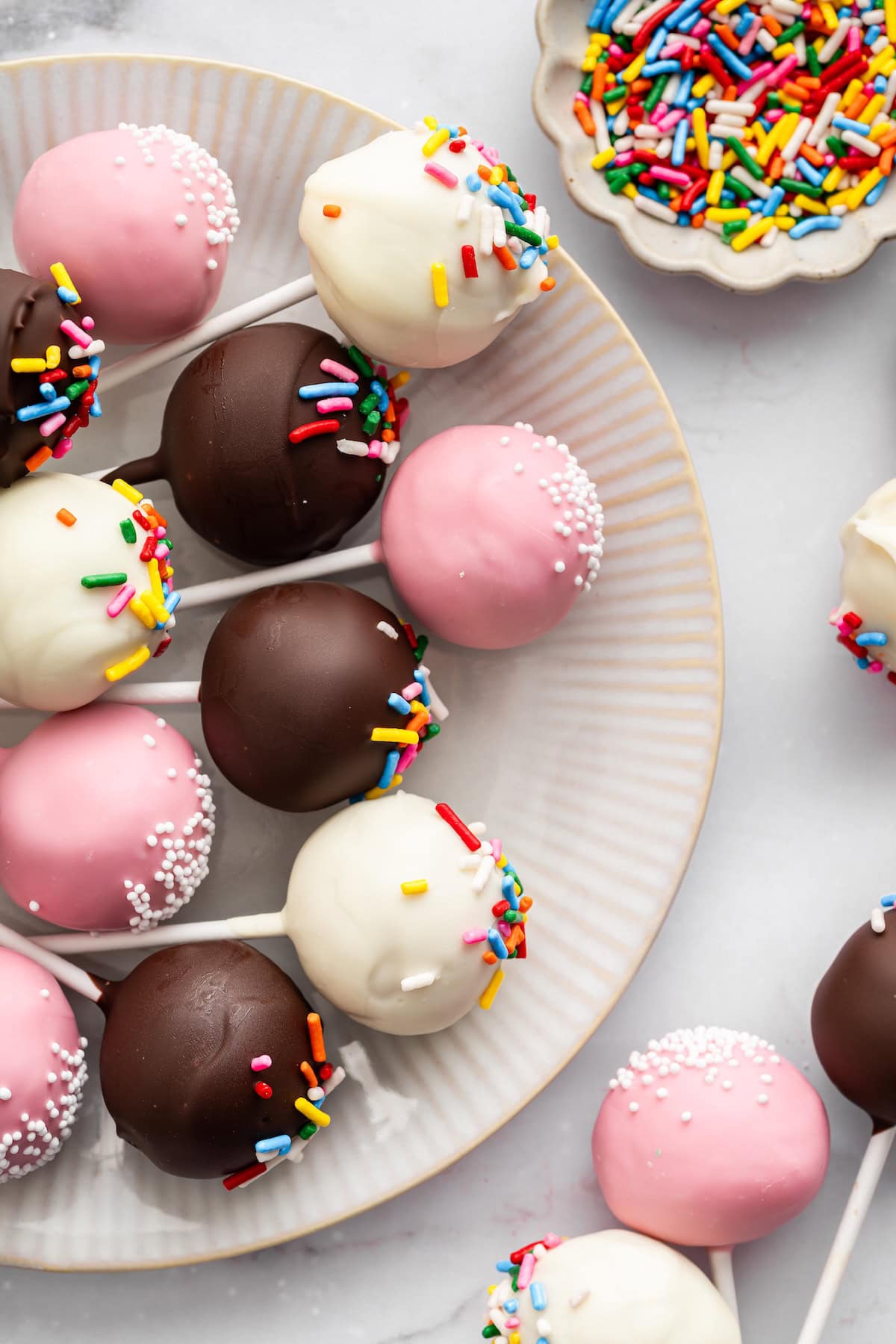 Assorted chocolate and pink cake pops decorated with colorful sprinkles on a plate.