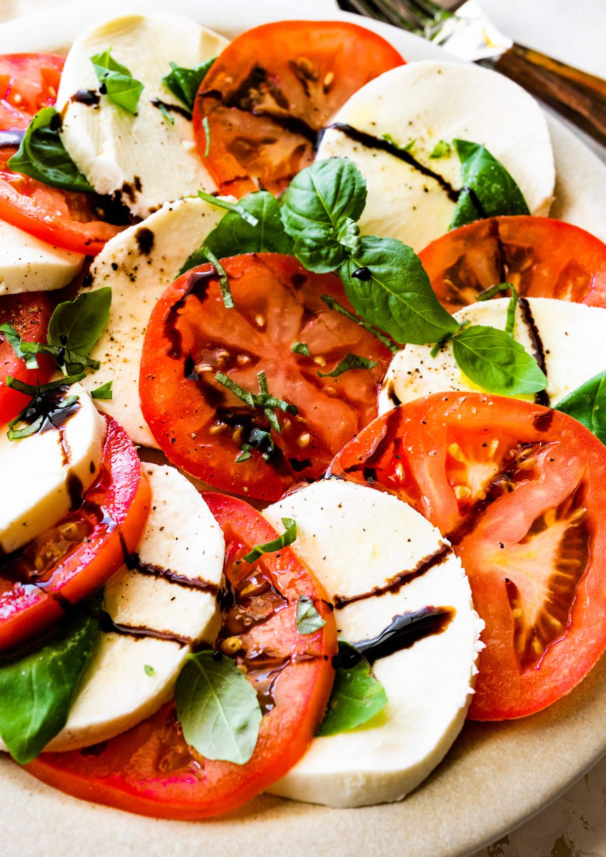 A caprese salad on a plate with sliced mozzarella cheese, sliced tomatoes, fresh basil, and a drizzle of balsamic vinegar.