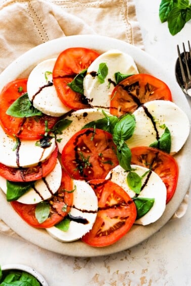 A caprese salad on a plate with sliced mozzarella cheese, sliced tomatoes, fresh basil, and a drizzle of balsamic vinegar.