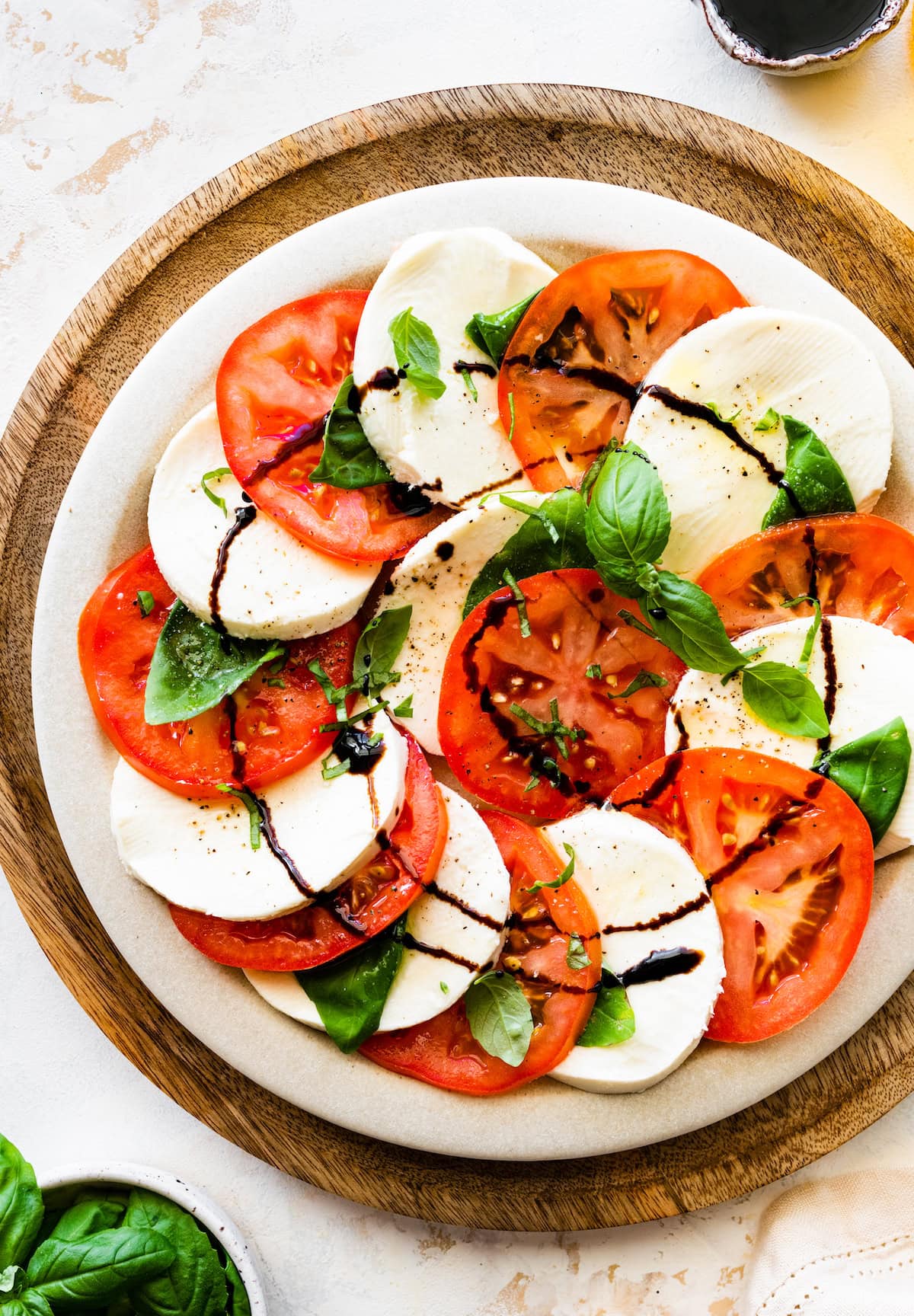 A caprese salad on a plate with sliced mozzarella cheese, sliced tomatoes, fresh basil, and a drizzle of balsamic vinegar.