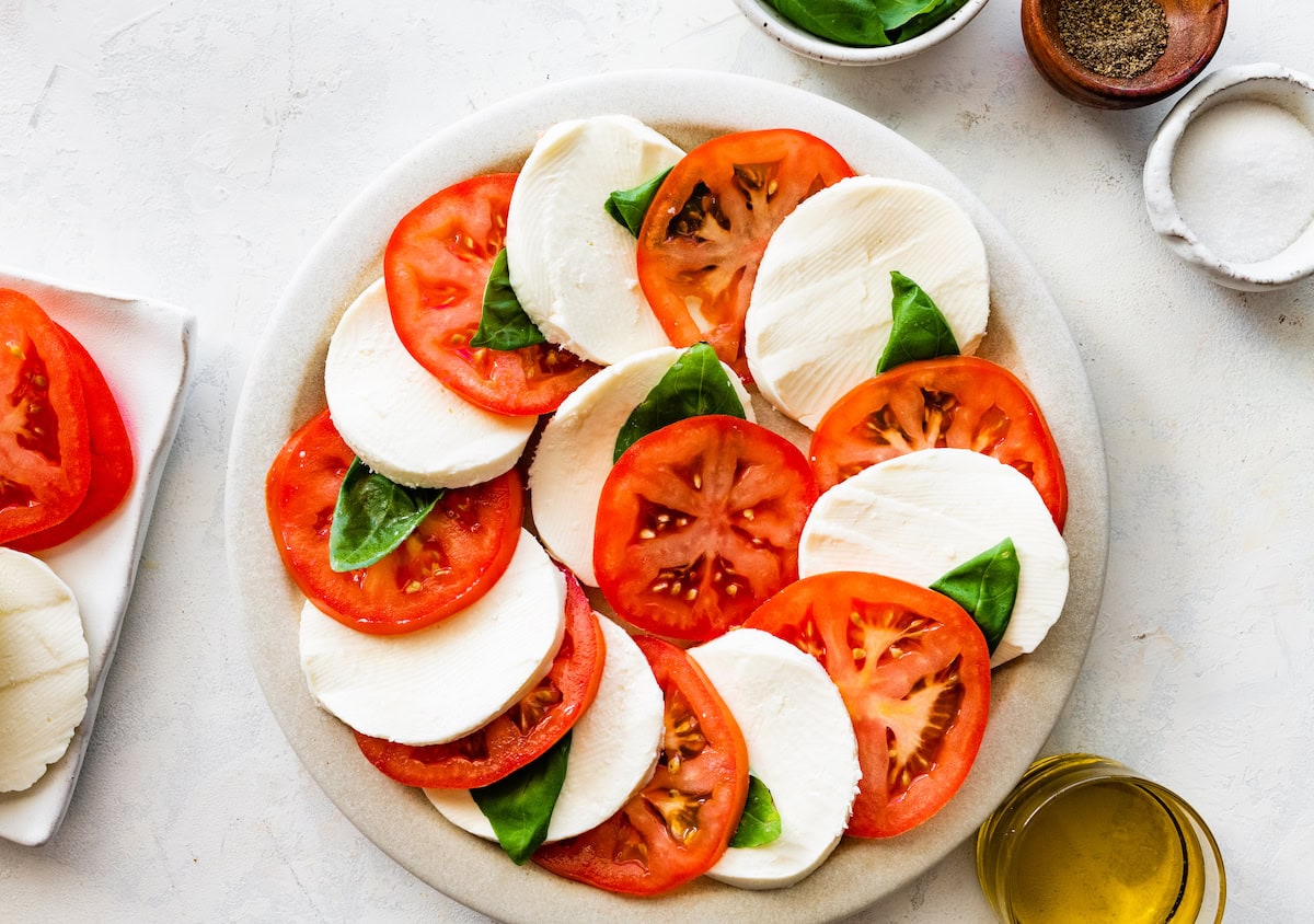 A caprese salad on a plate with sliced mozzarella cheese, sliced tomatoes, and fresh basil.