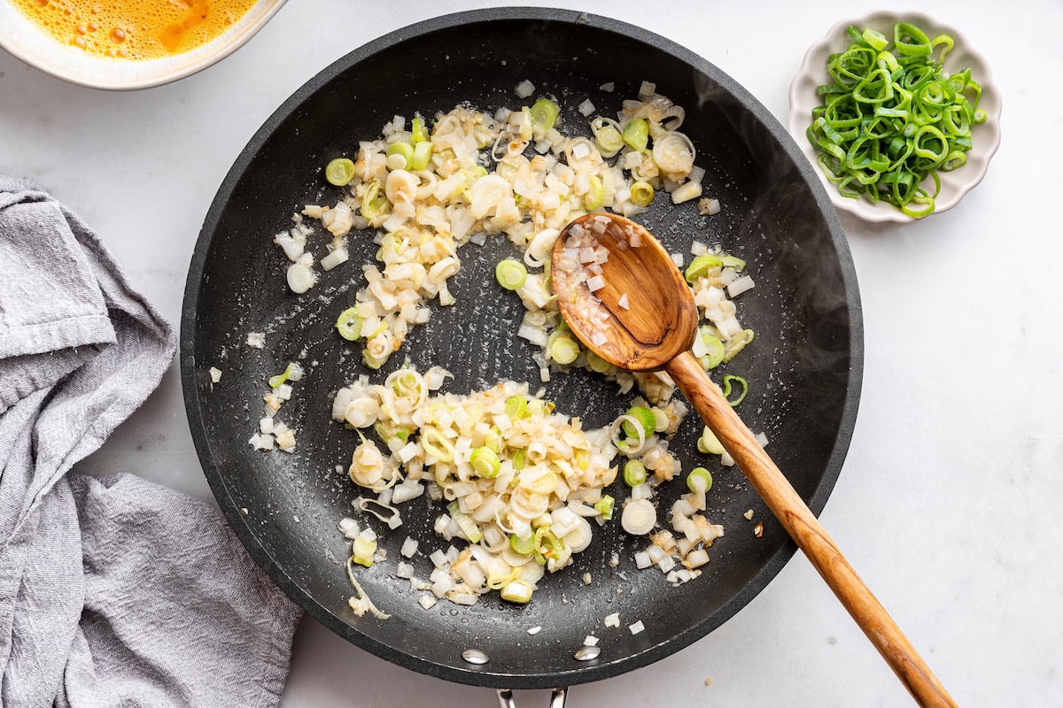 A wooden spoon in a skillet with onion and garlic.