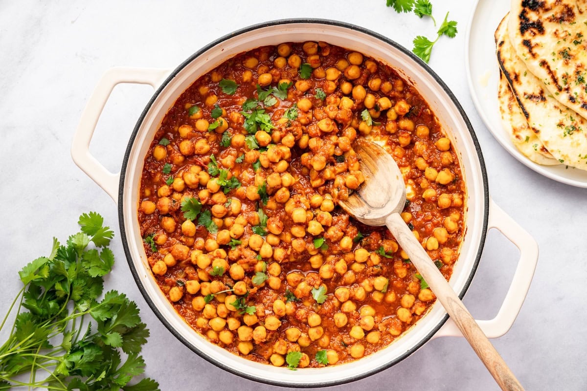 Thick and flavorful chana masala simmering on the stovetop with a wooden spoon.