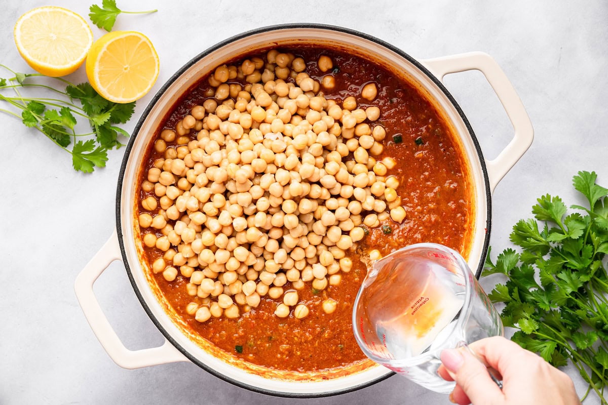 Draining chickpeas poured into simmering spiced tomato sauce to make chana masala.