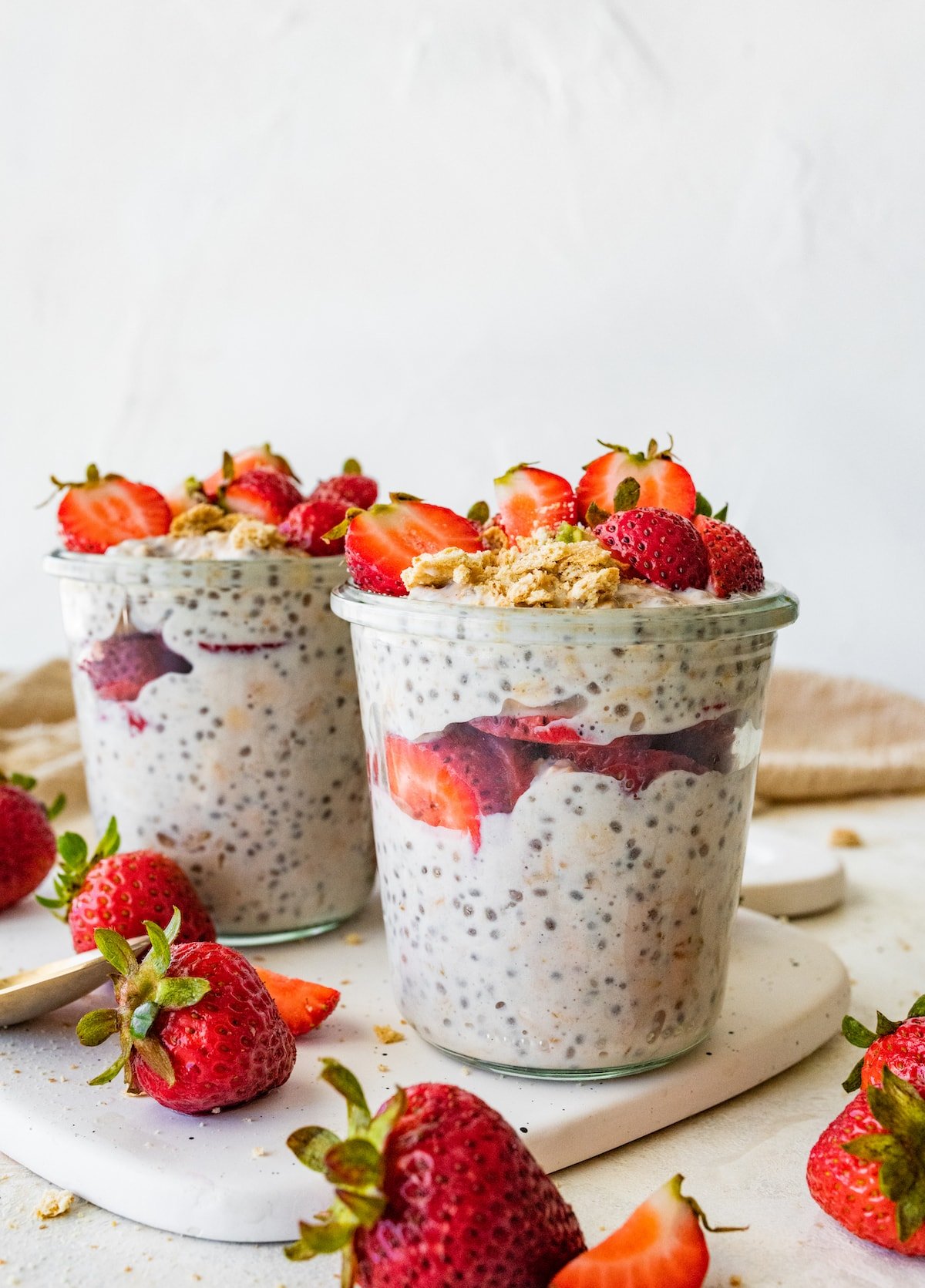 Two jars with strawberry cheesecake overnight oats topped with fresh strawberries.