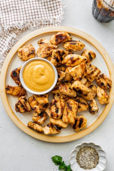 Plate of grilled chicken nuggets served with a small bowl of dipping sauce.