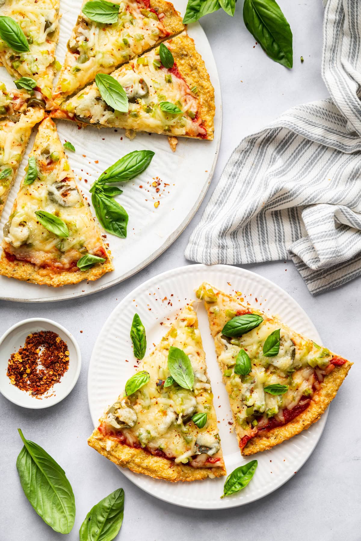 Sliced chicken crust pizza on plates with fresh basil and red pepper flakes.