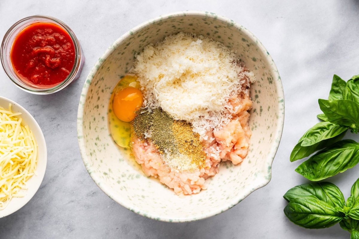 Mixing ground chicken, egg, Parmesan, and seasonings in a bowl for chicken crust.