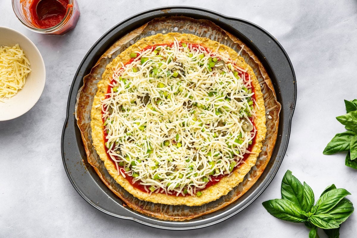 Chicken crust pizza topped with sauce, mozzarella cheese, peppers and jalapeños before baking.