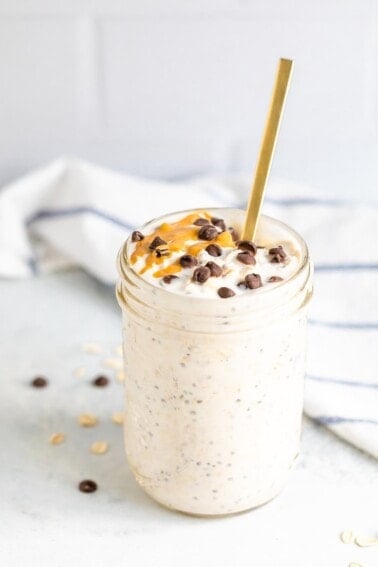 Chocolate chip overnight oats in a mason jar with a gold spoon. Topped with chocolate chips and a peanut butter drizzle.