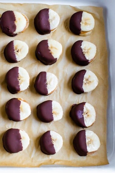 Chocolate peanut butter banana bites on a plate. Slices of banana sandwiched with peanut butter and dipped half in chocolate and frozen.