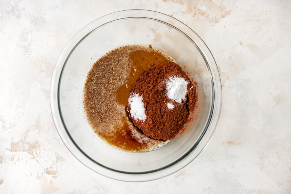 Almond butter, flax egg, maple syrup, cocoa powder, baking soda, salt, vanilla extract and peppermint extract in a glass mixing bowl.