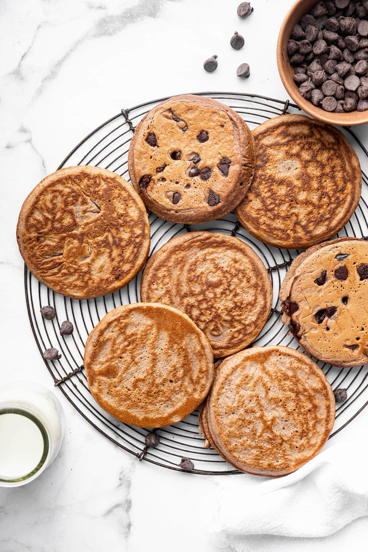 Chocolate protein pancakes cooling on a wire rack, some with chocolate chips.