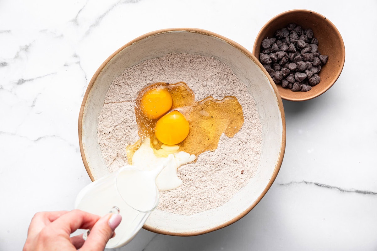 Adding eggs and almond milk into dry ingredients for chocolate protein pancake batter.