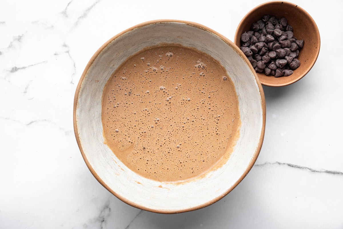 Mixing bowl filled with chocolate protein pancake batter, chocolate chips on the side.