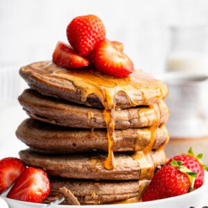 Stack of fluffy chocolate protein pancakes topped with strawberries and nut butter drizzle.