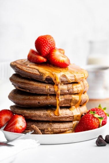 Stack of fluffy chocolate protein pancakes topped with strawberries and nut butter drizzle.