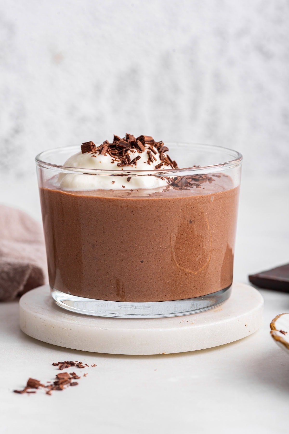Chocolate protein pudding in a glass cup topped with whipped cream and shaved chocolate.