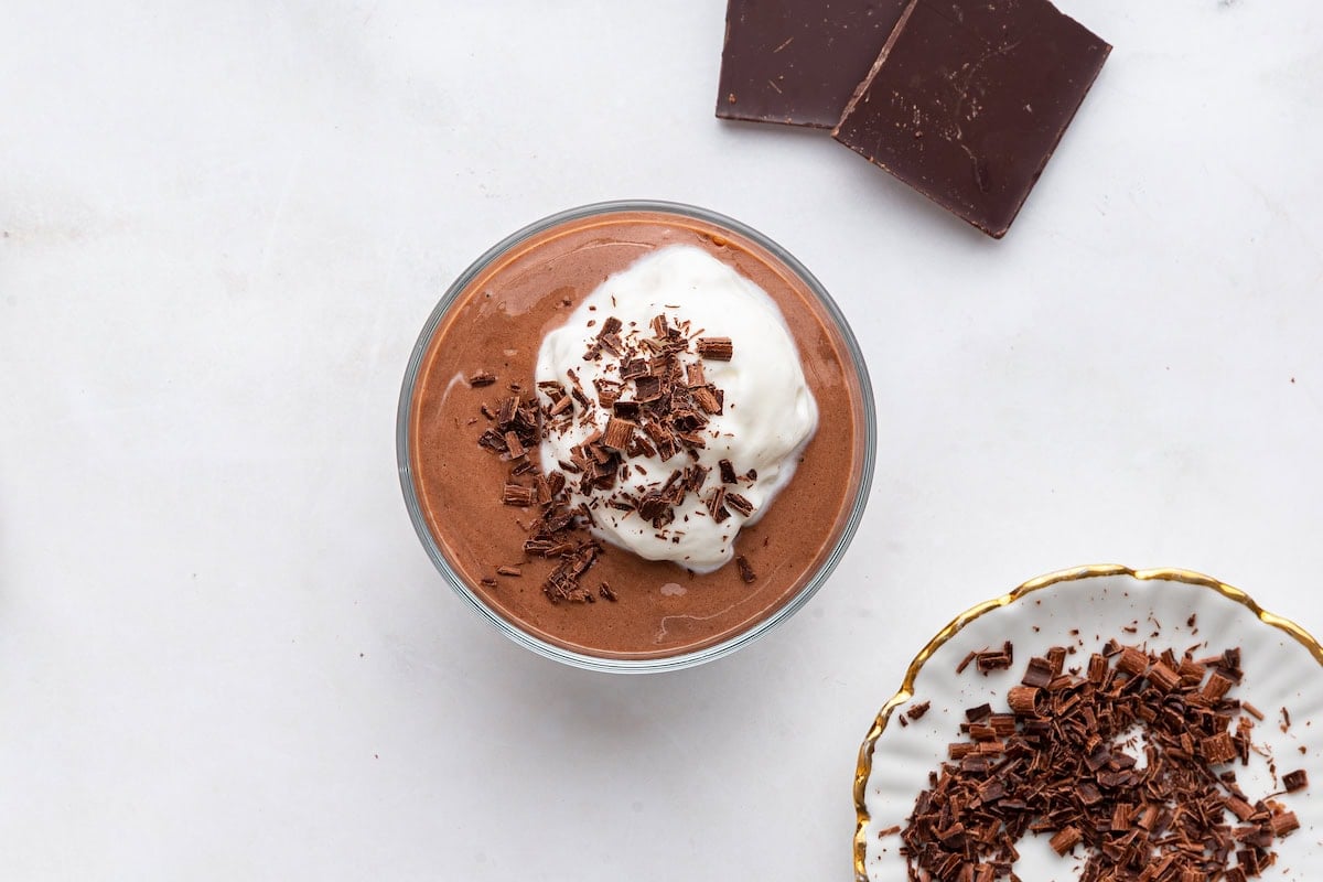 Chocolate protein pudding in a glass cup topped with whipped cream and shaved chocolate.
