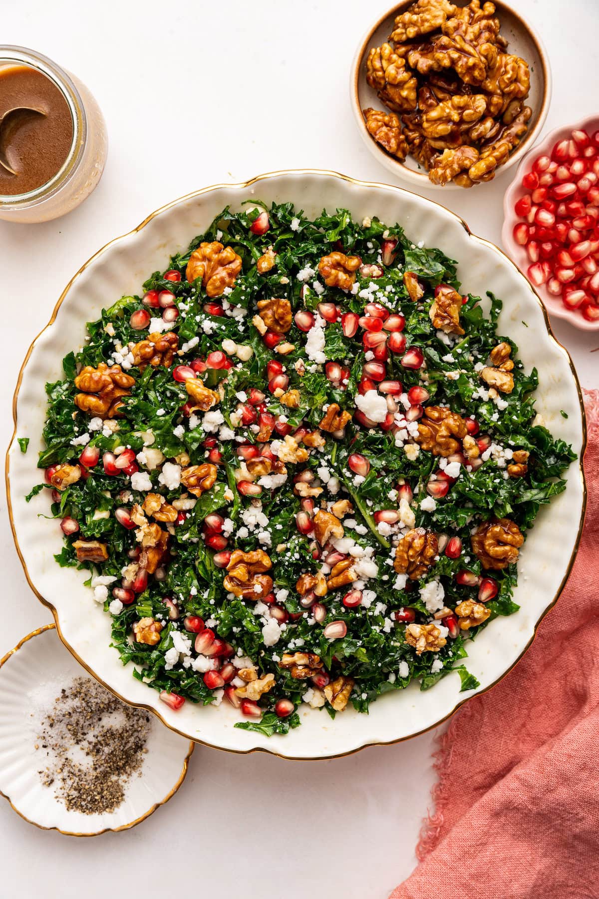A kale salad topped with fresh pomegranate, goat cheese and candied walnuts. The salad is served in a white bowl.