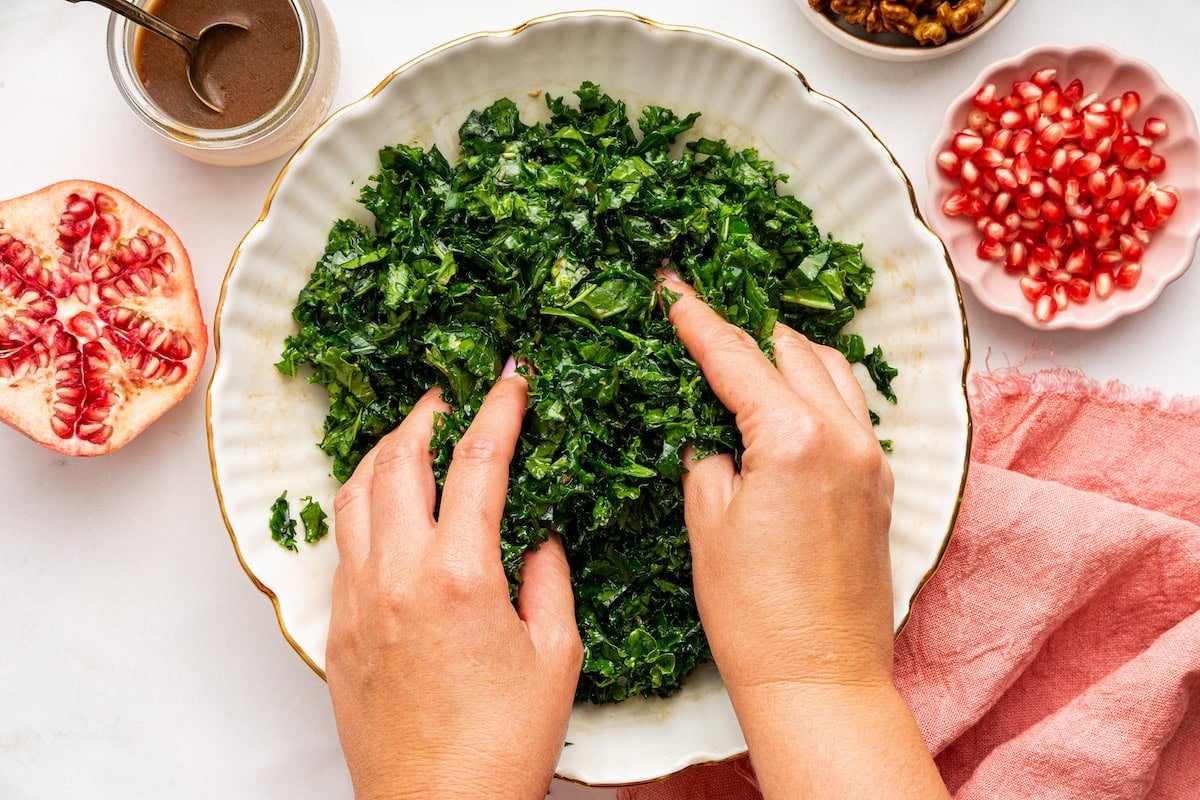 A woman's hands massaging kale with dressing in a white serving bowl.