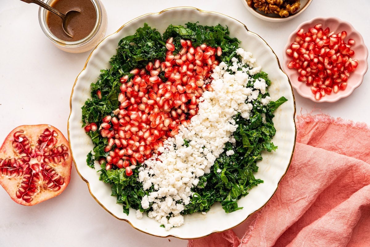 A bed of kale topped with fresh pomegranate seeds and goat cheese all served in a white bowl.