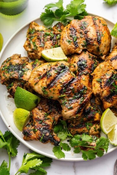 Cooked cilantro lime chicken thighs served on a plate topped with fresh cilantro and lime wedges.