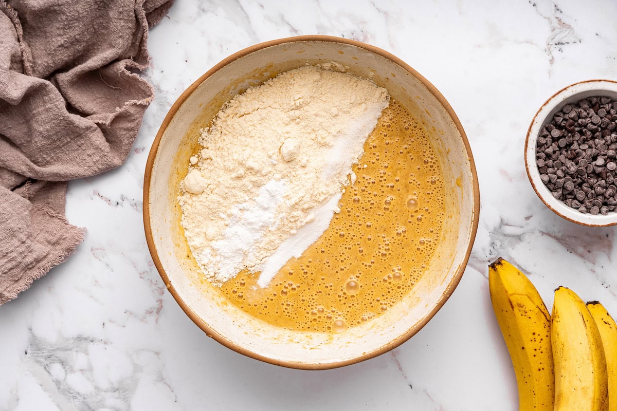 Coconut flour added to a large bowl of wet ingredients for coconut flour banana bread.