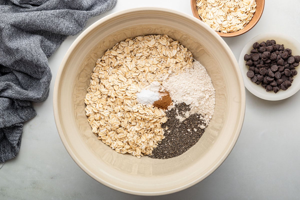 The dry ingredients for the chocolate chip cookie granola in a ceramic mixing bowl: rolled oats, chia seeds, oat flour, cinnamon and baking soda.
