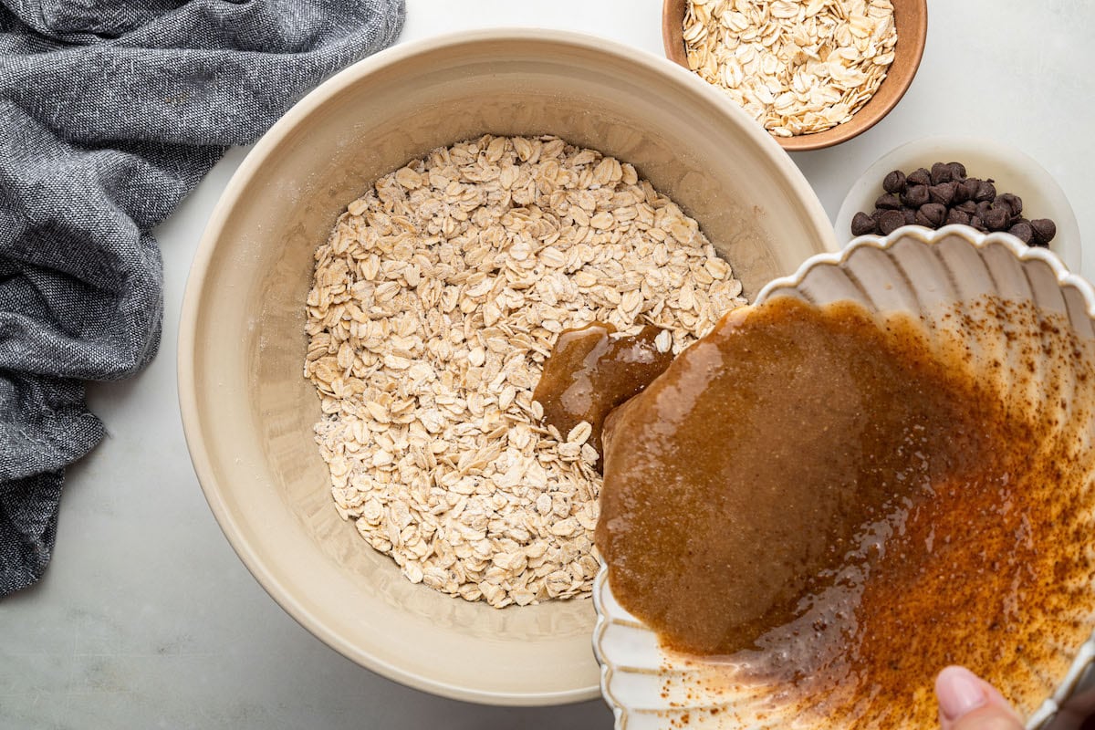 The wet ingredients being poured over the dry ingredients in a ceramic bowl for the cookie granola.