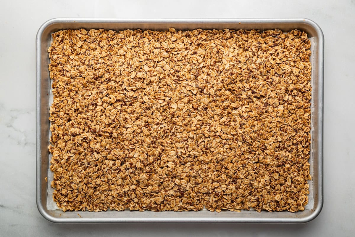 The baked cookie granola spread out on a silver baking sheet lined with parchment paper.
