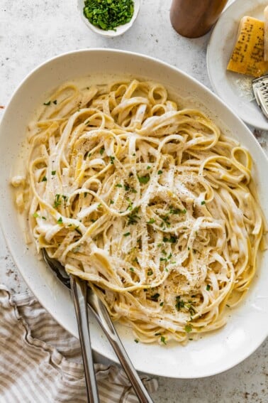 Serving bowl of cottage cheese Alfredo fettuccine topped with parmesan, parsley, and black pepper.