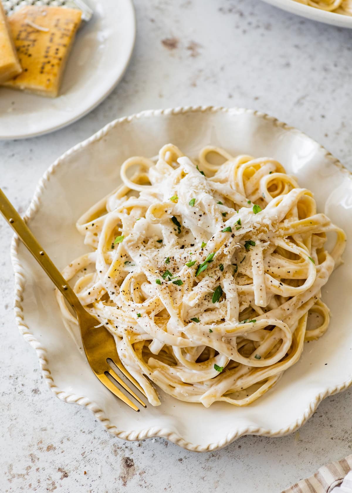 Plate of fettuccine tossed in creamy cottage cheese Alfredo sauce topped with parmesan and pepper.