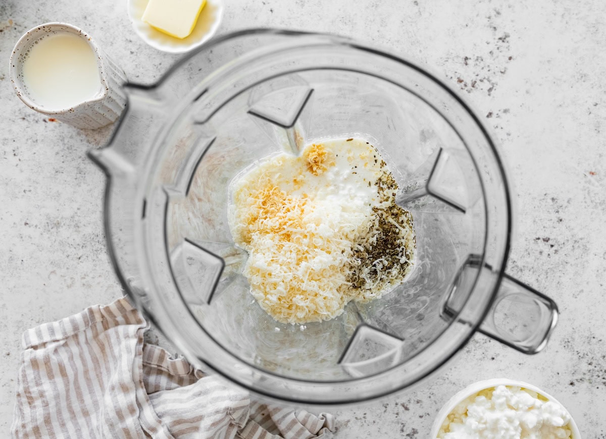 Cottage cheese, parmesan, milk, and seasonings added to a blender before blending into Alfredo sauce.