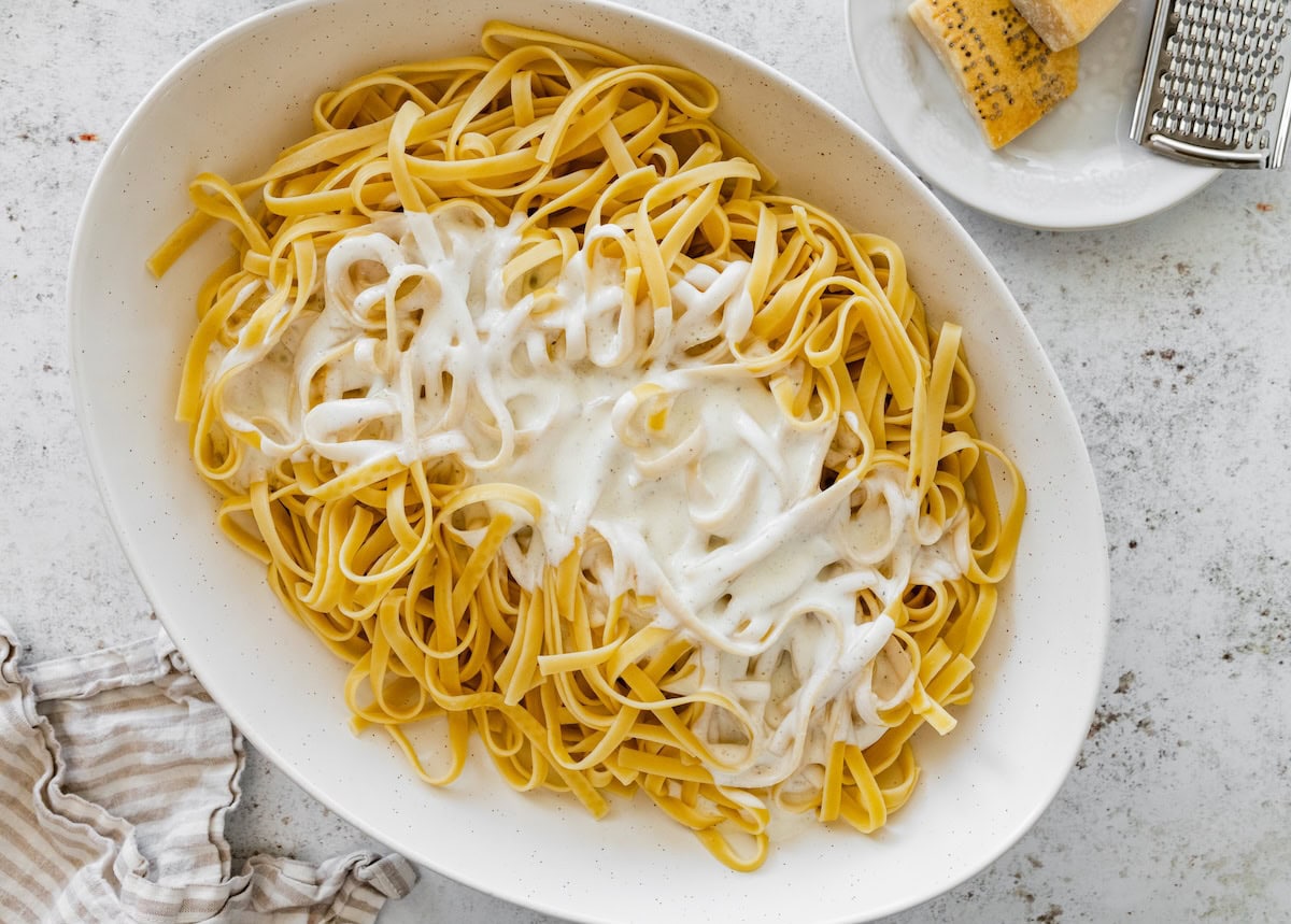 Cooked fettuccine noodles topped with freshly poured cottage cheese Alfredo sauce before mixing.