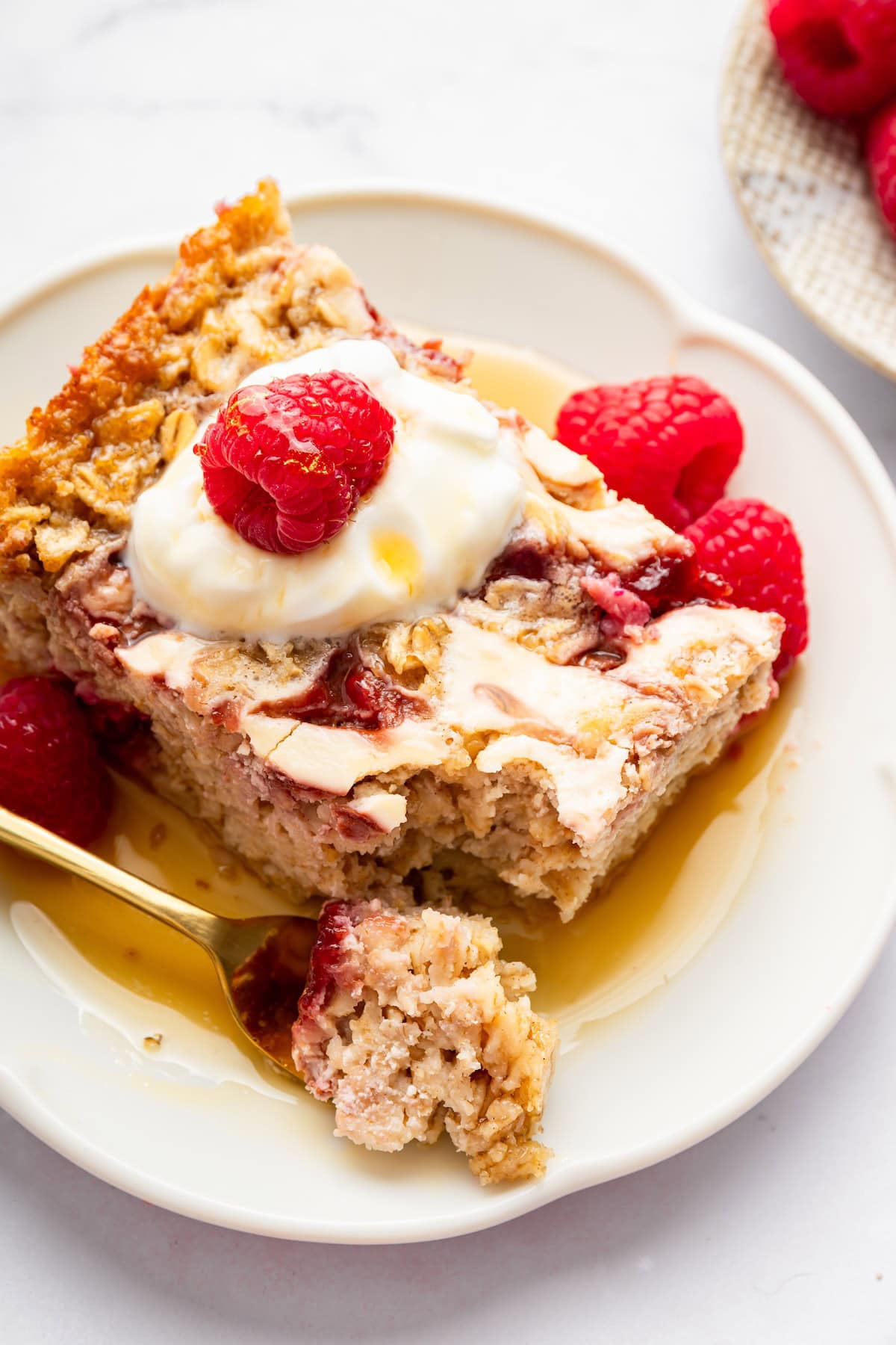 Slice of raspberry cottage cheese baked oatmeal topped with yogurt, maple syrup and raspberries.