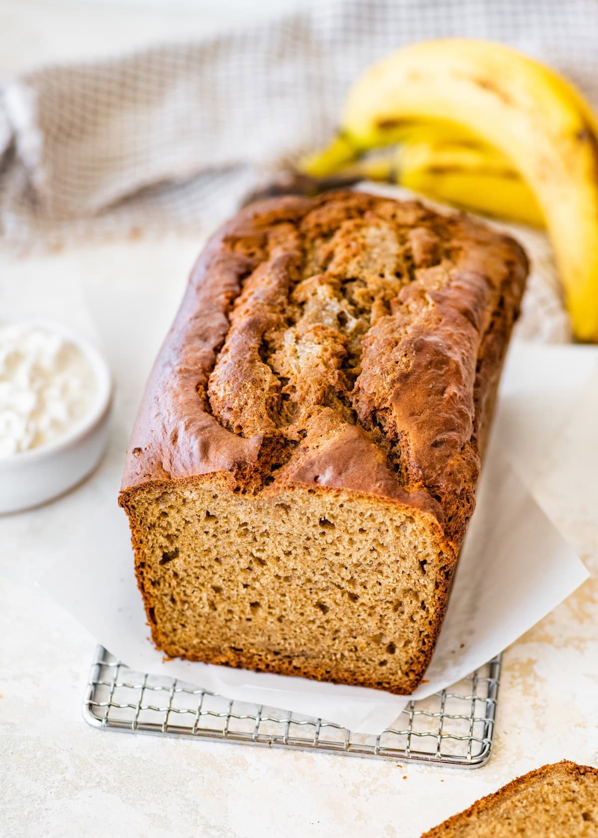 Whole loaf of cottage cheese banana bread on parchment with cottage cheese and bananas nearby.